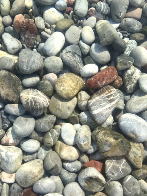 Tilos Island stones rolling in waves of clear ocean water